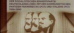 Das Buchcover zeigt ein sepia gefärbtes historisches Foto einer Rede von Erich Honecker . Hinter ihm applaudieren ihm Parteimittglieder. Über ihm im Saal an der Wand hängen die Profile von großen Kommunisten.